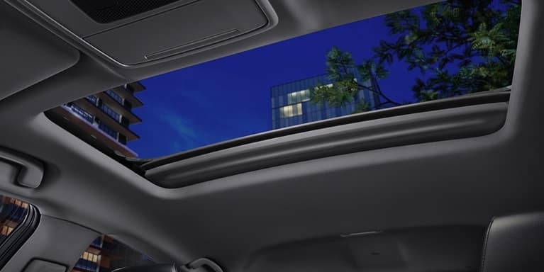 2026 Honda Accord detail of the one touch power moonroof parked on the rooftop of parking structure at night, with highrise buildings in the background.